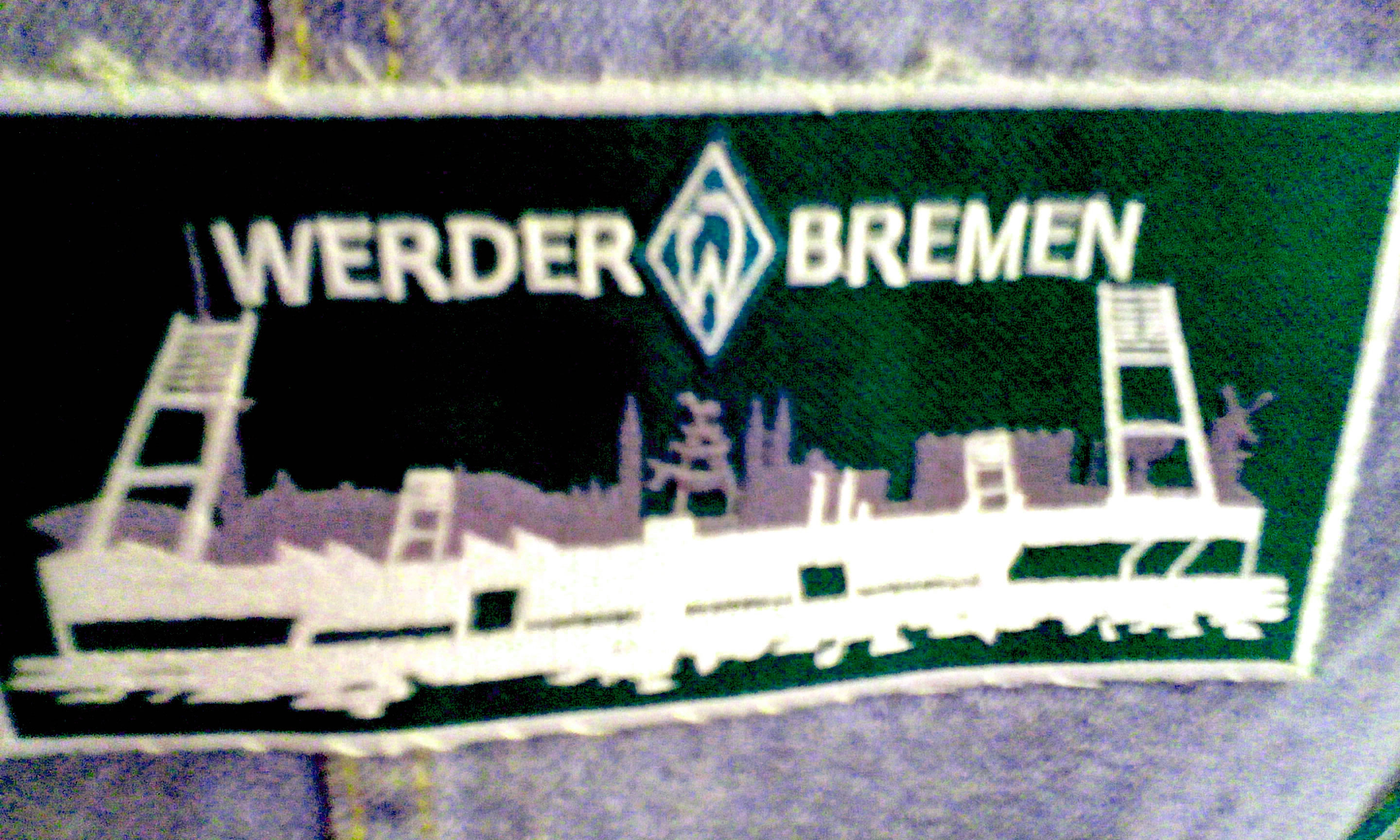 Ein kleiner grün weisser Stoffaufnäher mit der Silhouette des Weser Stadions, Bremens und den Bremer Stadtmusikanten